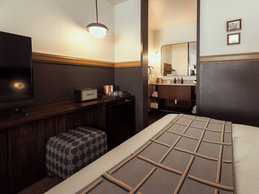 A hotel room with a bed, a television, a minibar, and a bathroom visible through an open door.