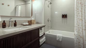 Un baño con ducha, bañera, lavabo con espejo y artículos de aseo.