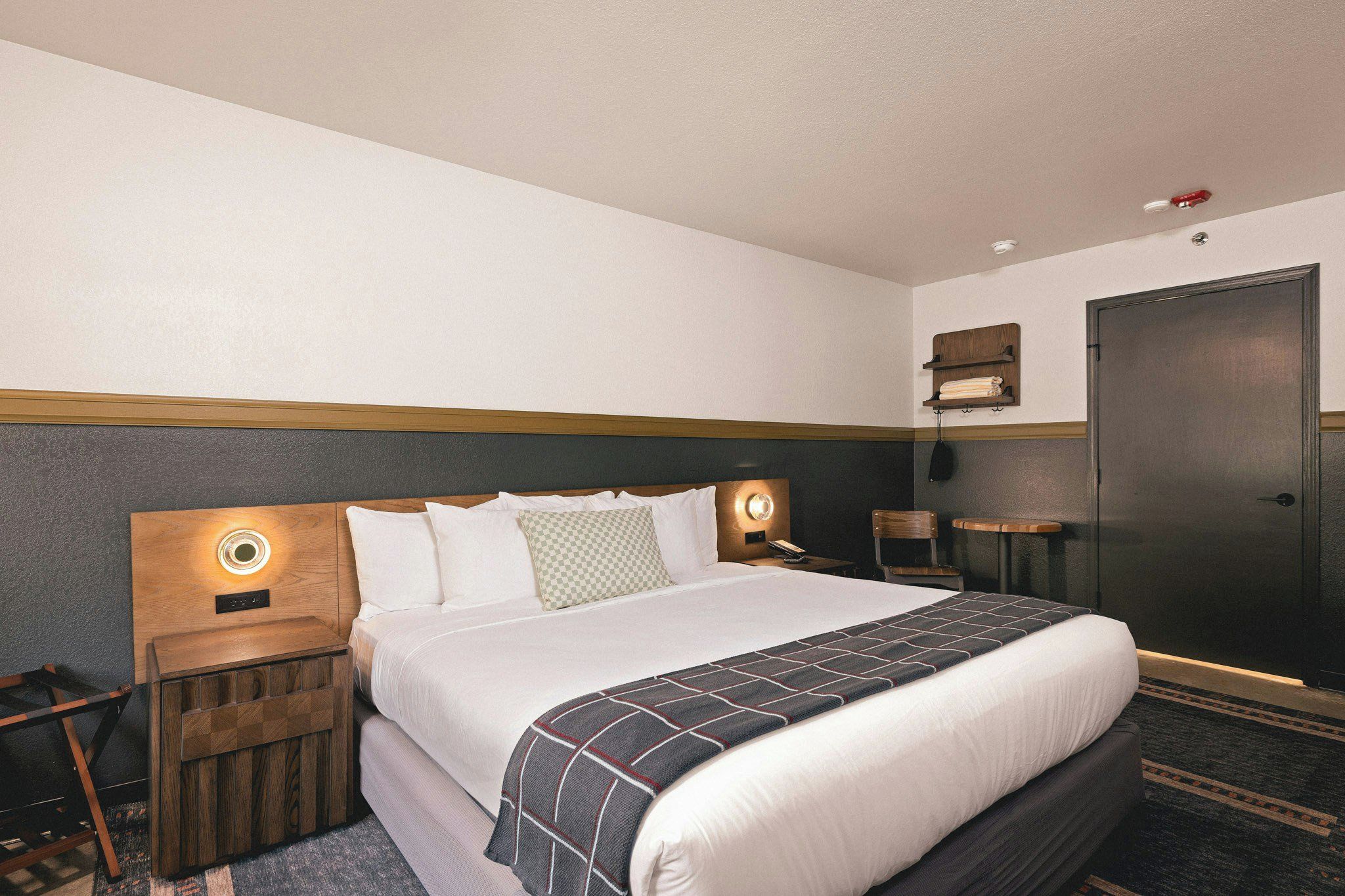 A hotel room with a bed, bedside tables, a wardrobe, and a wall-mounted shelf.