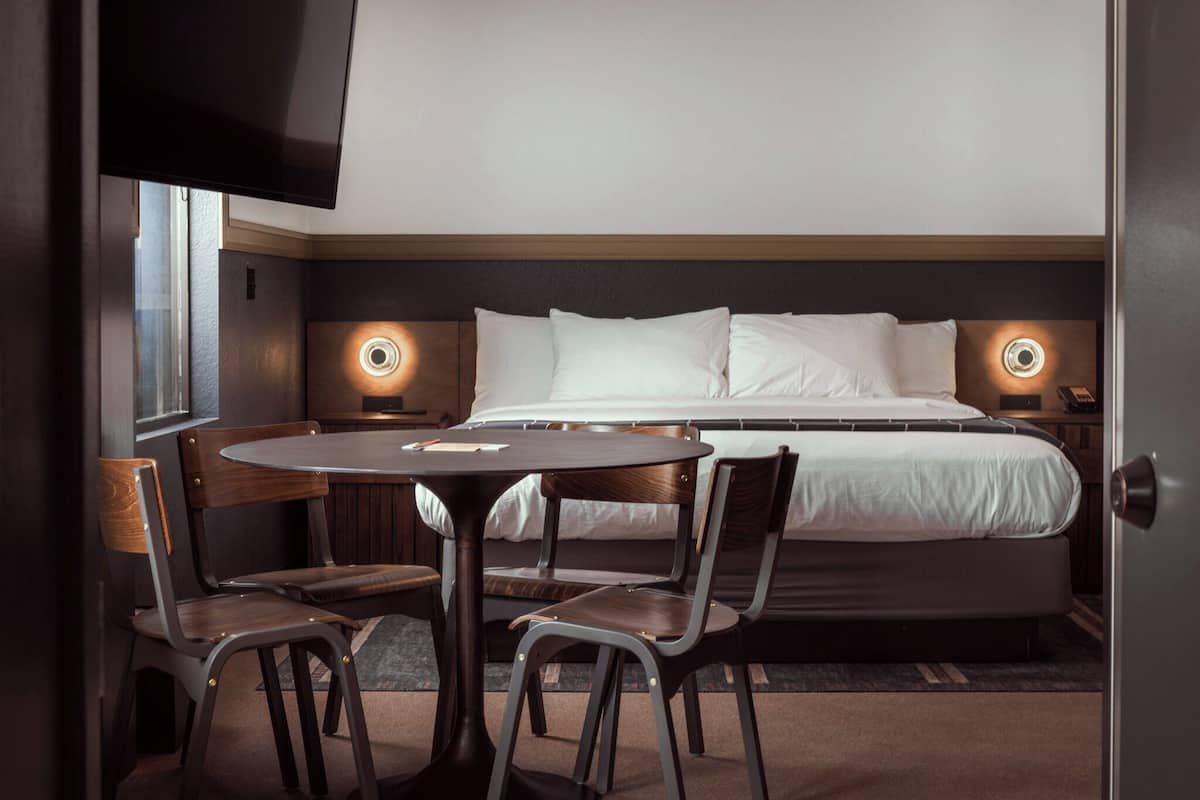 A hotel room with a bed, bedside tables, a round table, and two chairs.