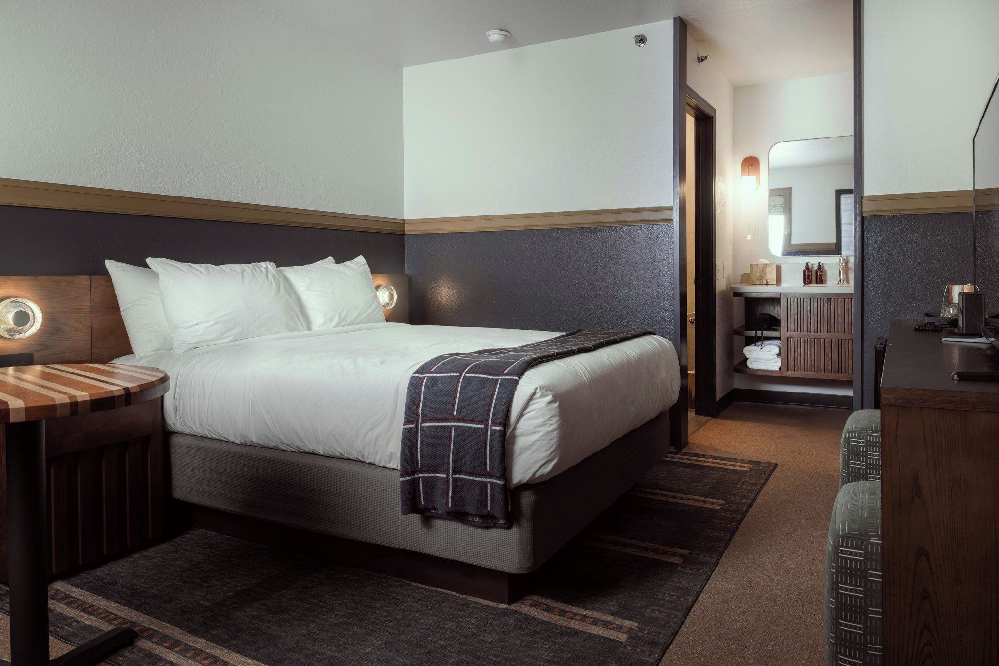 A hotel room with a bed, bedside table, and a mirror.