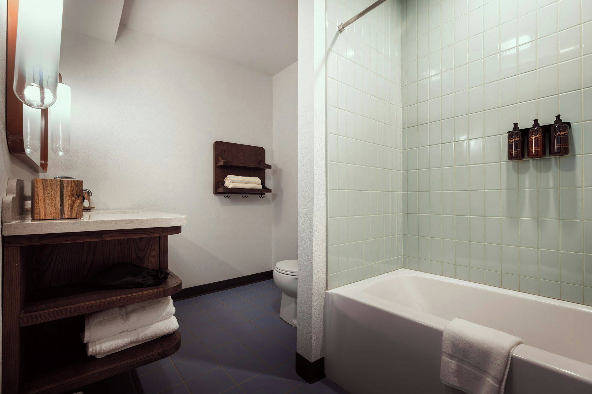 Un baño con bañera, inodoro, tocador de madera y repisa con toallas.