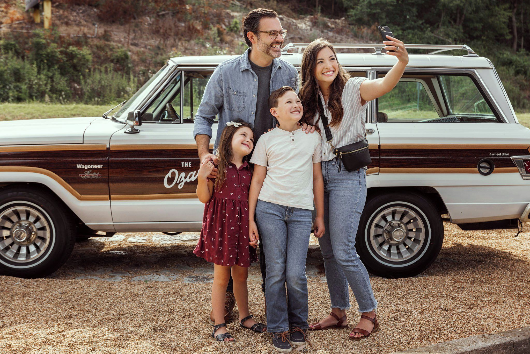 Una familia tomándose un selfie frente a un coche antiguo con los rótulos 'Wagoneer' y 'The Ozarks'.