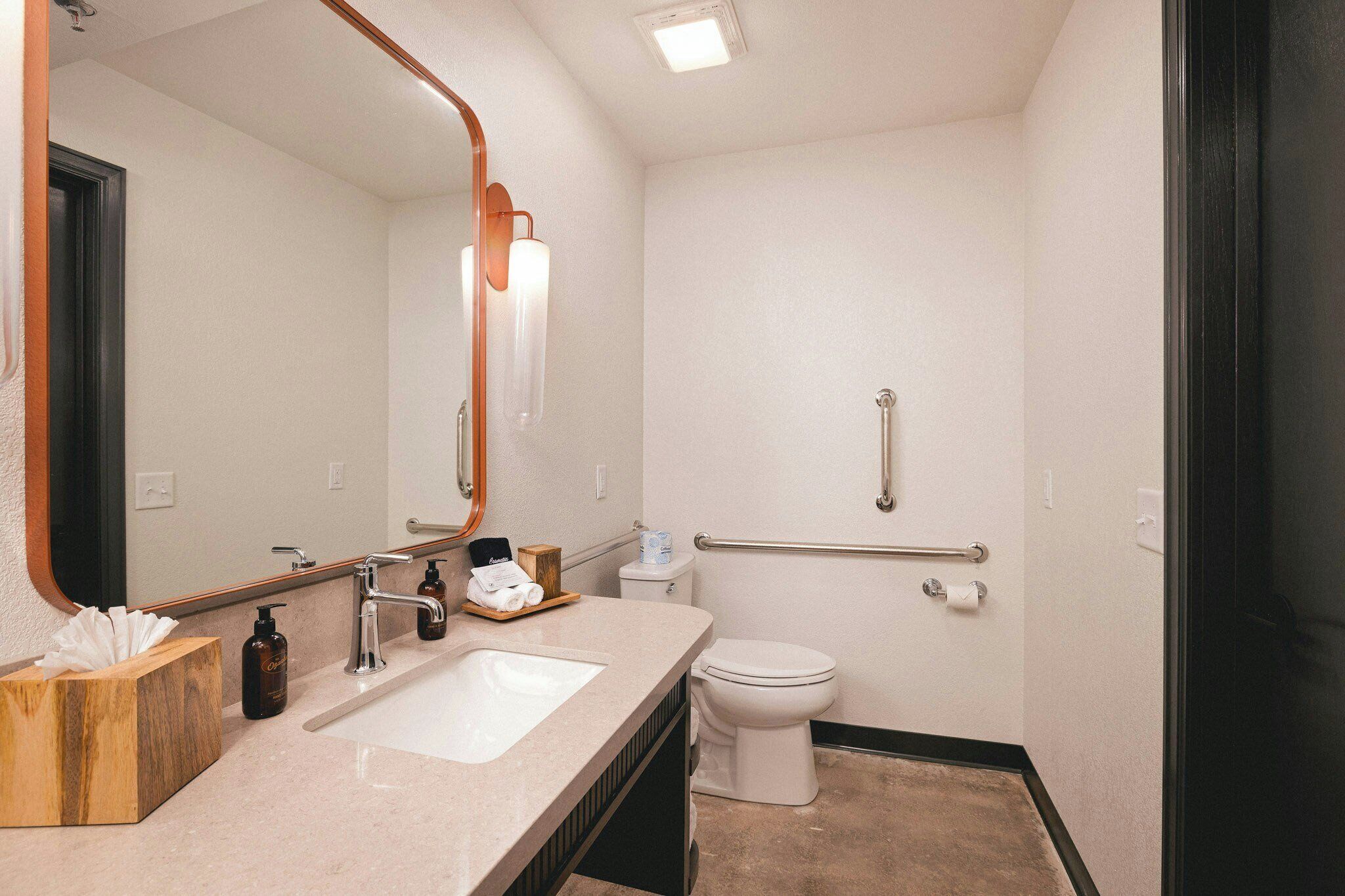 A bathroom with a sink, mirror, toilet, and grab bar.