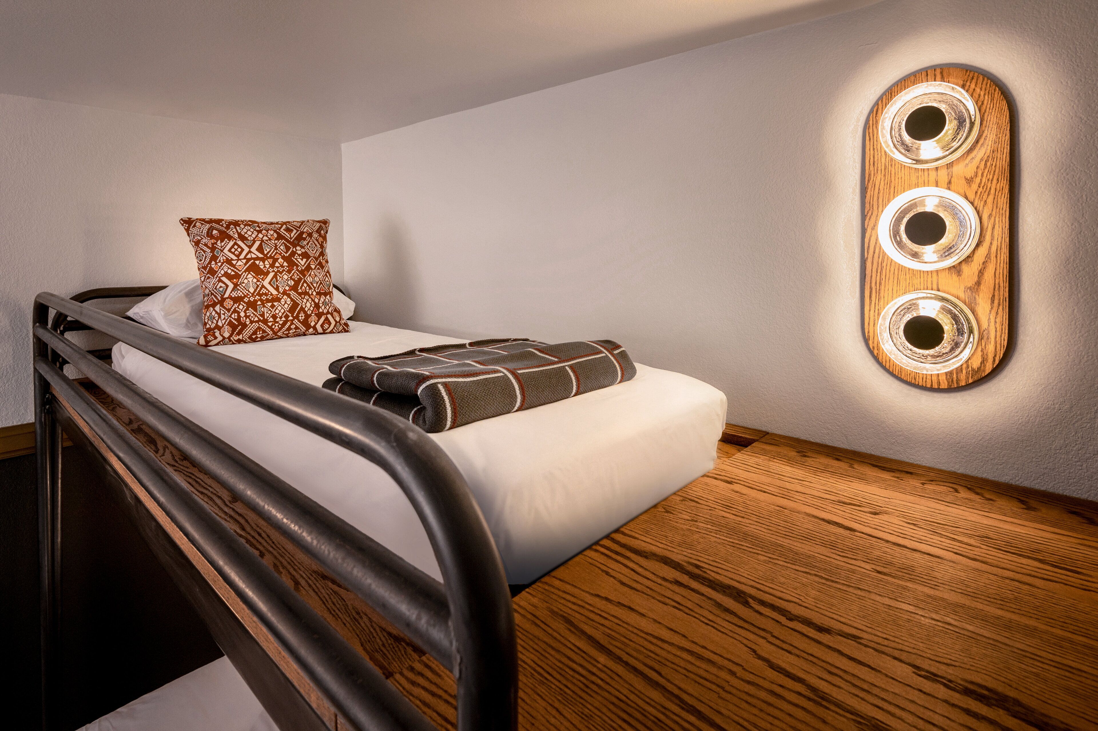A single bed with a headboard, a patterned pillow, a blanket, and a wall-mounted light fixture.