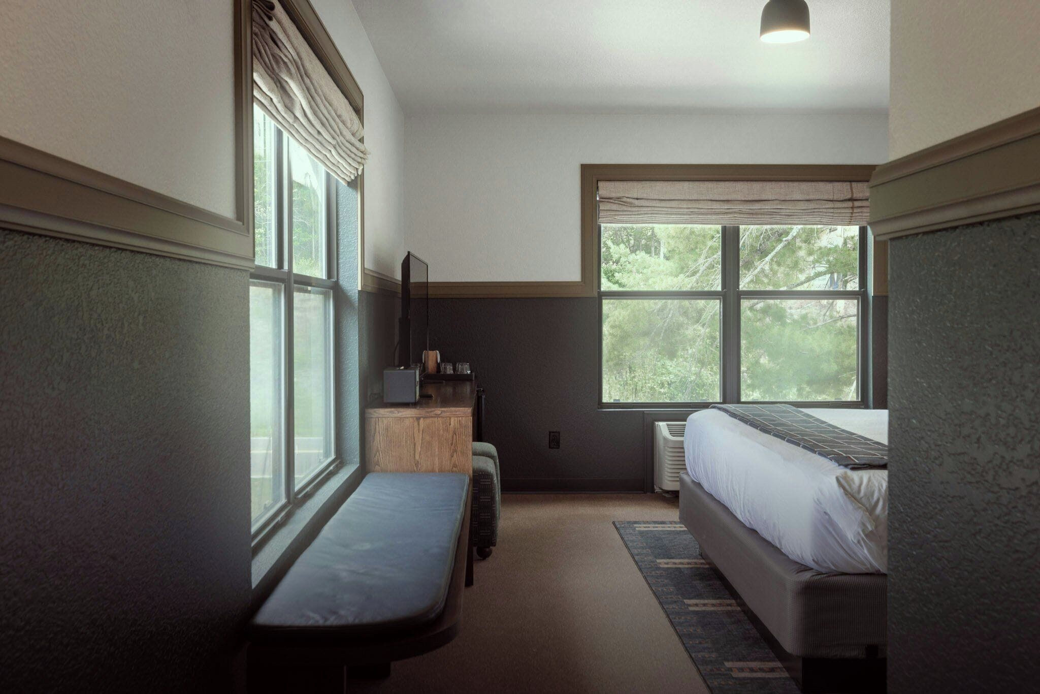 A bedroom with a bed, a bench, a dresser, and a window with a view of trees.