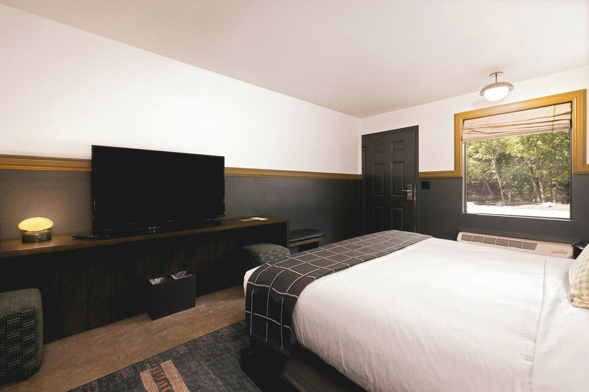 Een hotelkamer met een bed, een bureau met televisie, een kledingkast en een raam met uitzicht op bomen.