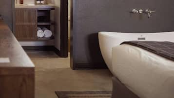 Una habitación de hotel con cama, mesita de noche, espejo y baño visible a través de una puerta abierta.