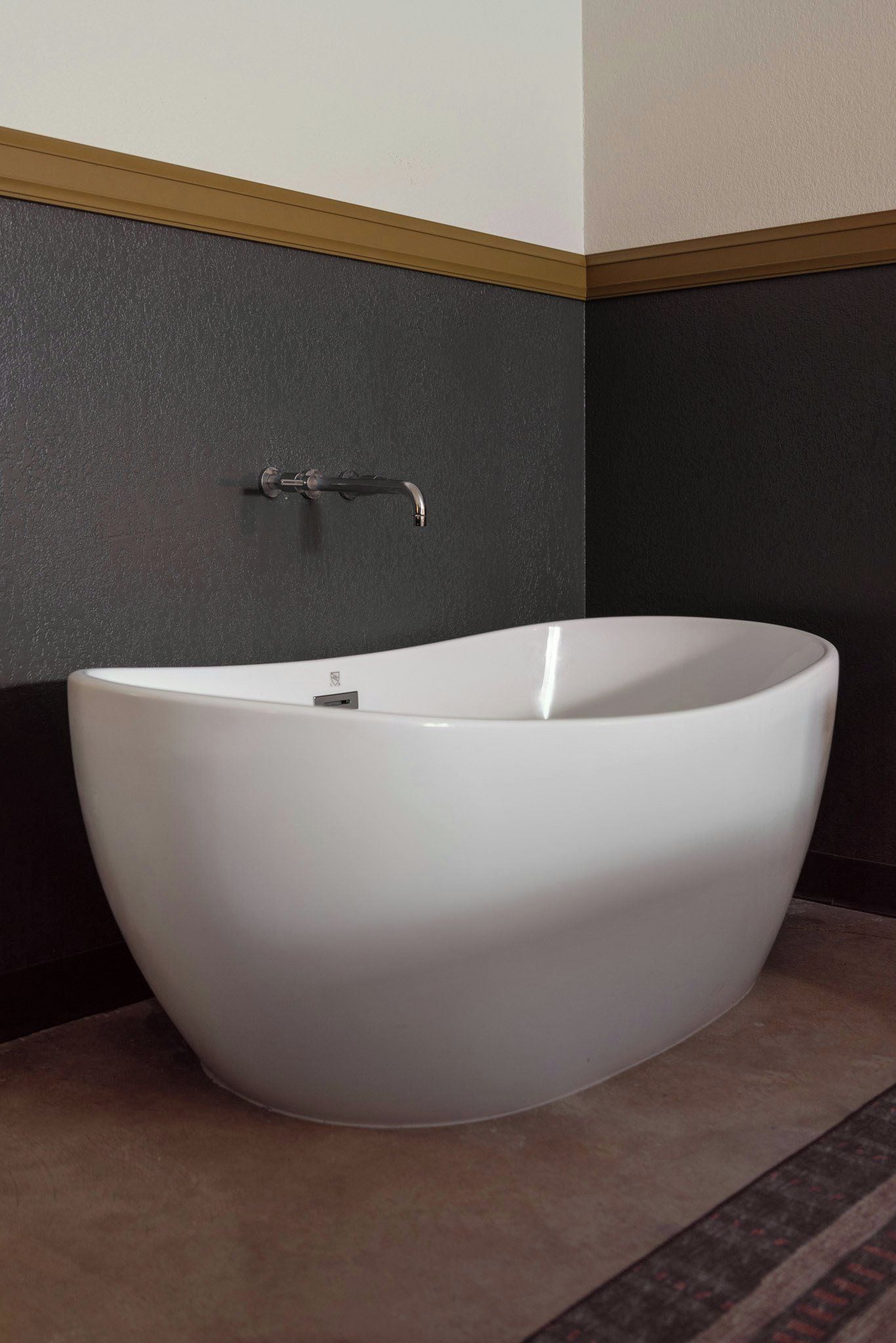 Een moderne badkamer met een vrijstaand bad, donkere muren met structuur en contrasterende, lichtgekleurde afwerking.
