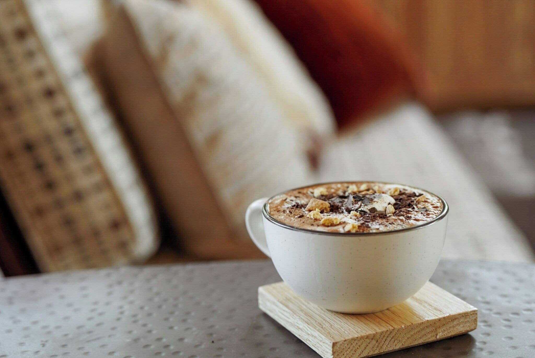 A white cup of hot beverage on a wooden coaster.