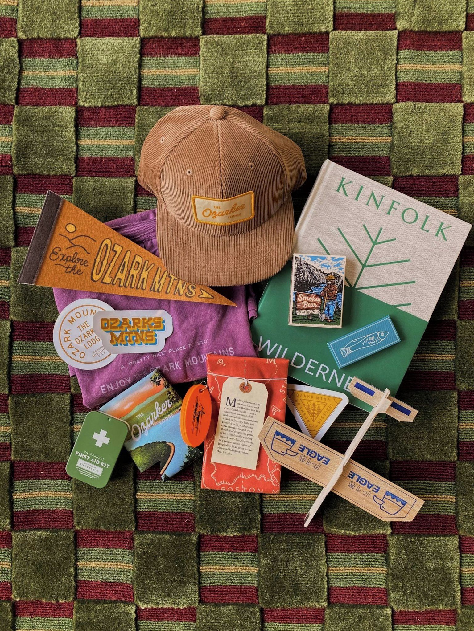 A collection of travel-related items including a cap, a book, a map, and various stickers on a textured fabric background.