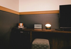 A corner of a room with a dark wall, a wooden desk, a small table with a lamp, a television, and a chair. - The Ozarker Lodge (Branson)