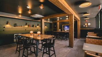 Un interior de restaurante con una mesa de comedor de madera, sillas negras y una zona de bar con taburetes.