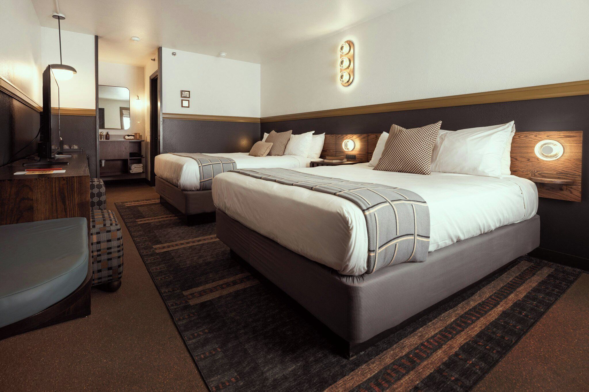 A hotel room with two beds, a desk, a chair, and a small seating area.