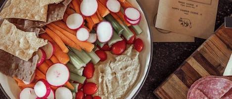 A plate with hummus, vegetables, crackers, and sliced salami.