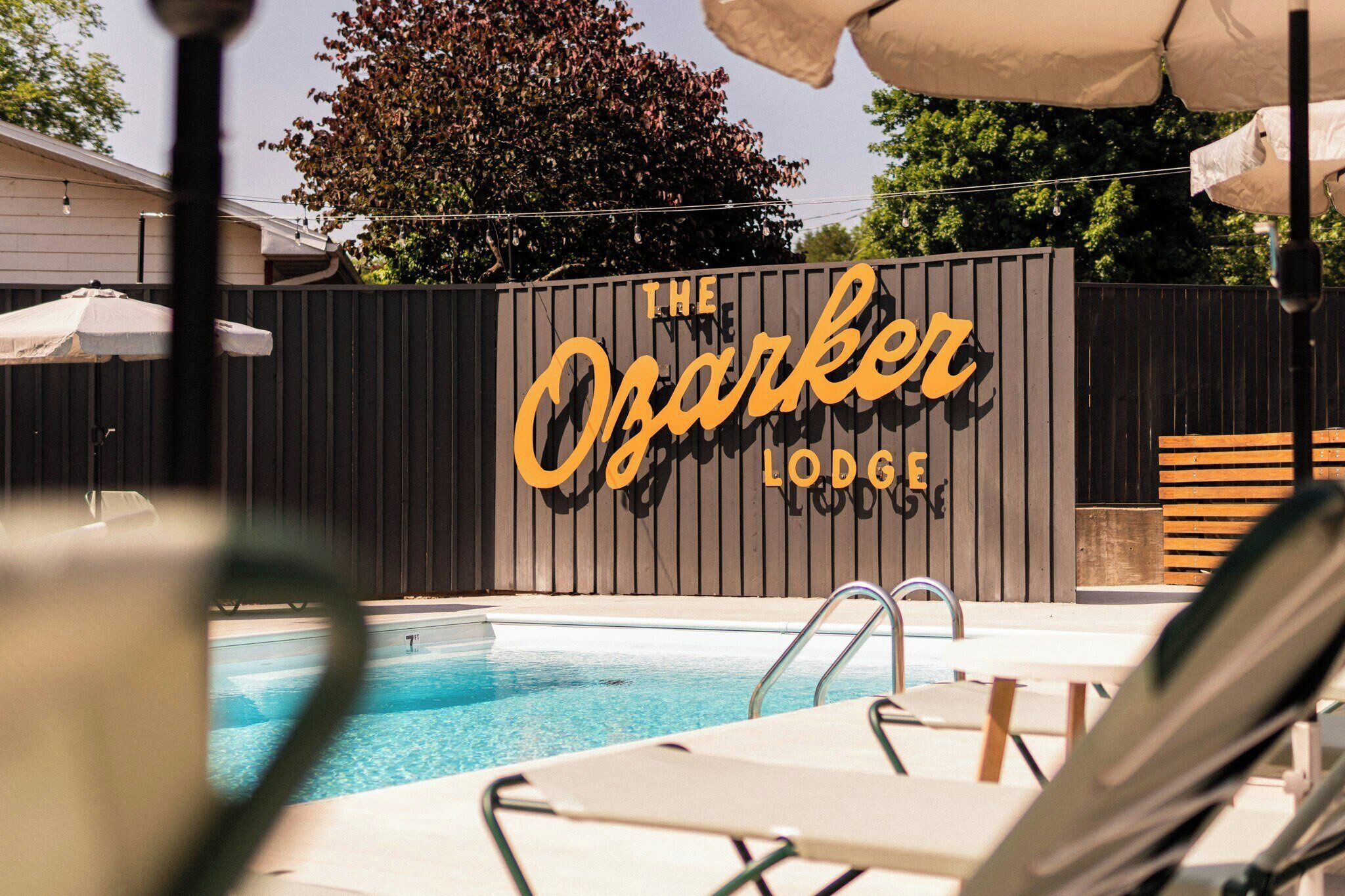 Una piscina con sillones de descanso y una cerca de madera con el letrero 'The Ozarker Lodge'.