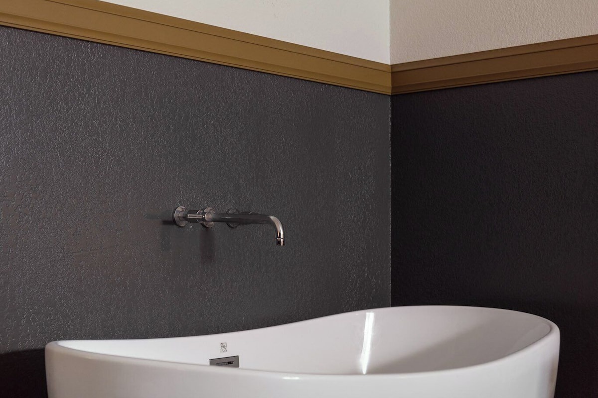 A modern bathroom with a freestanding bathtub, dark wall paneling, and a wooden trim.