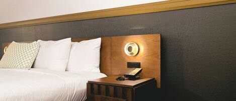 A hotel room with a bed, a bedside table with a lamp, and a wall-mounted phone.