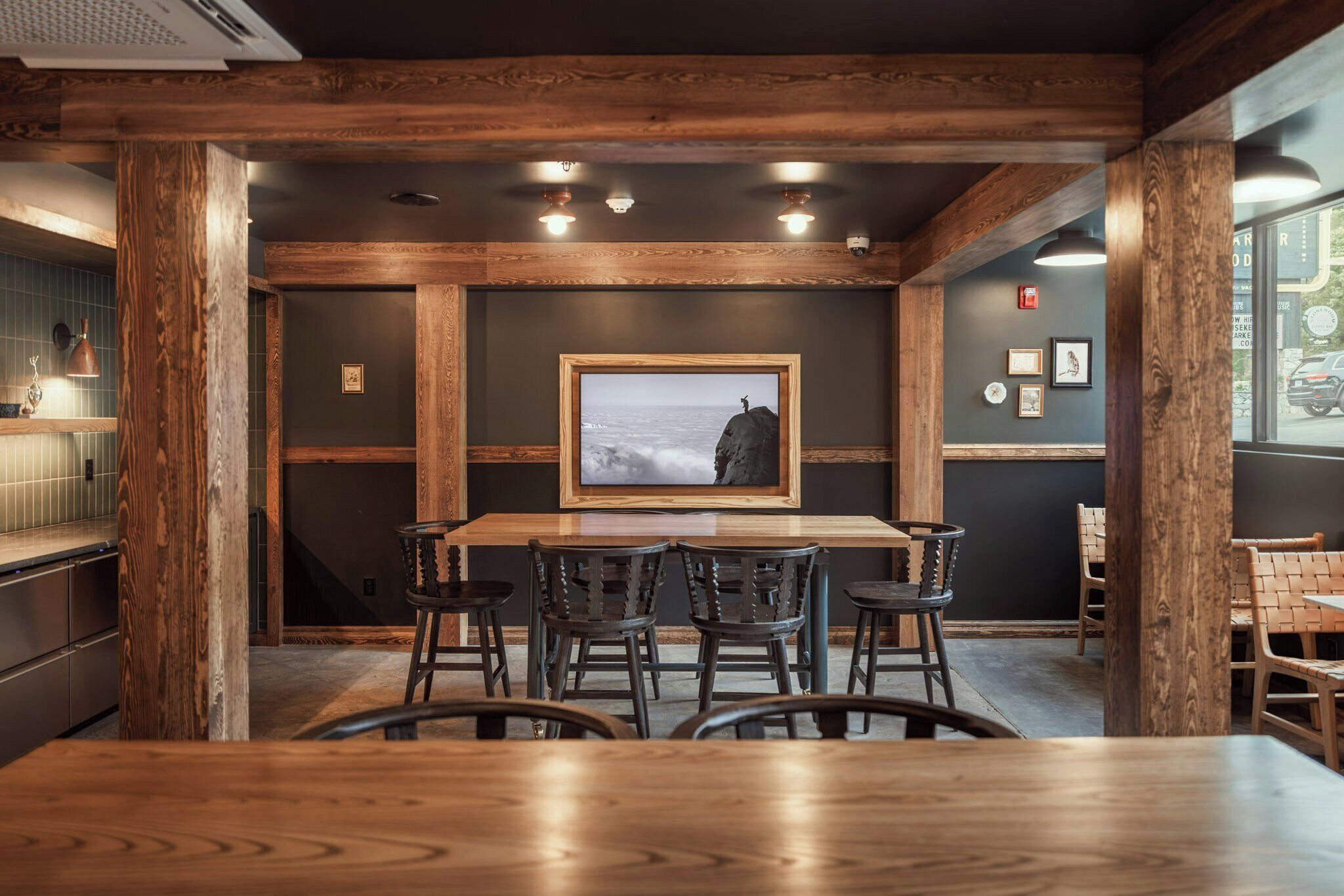 Interior de un restaurante con barra de madera, diversas opciones de asientos y un cuadro en la pared.