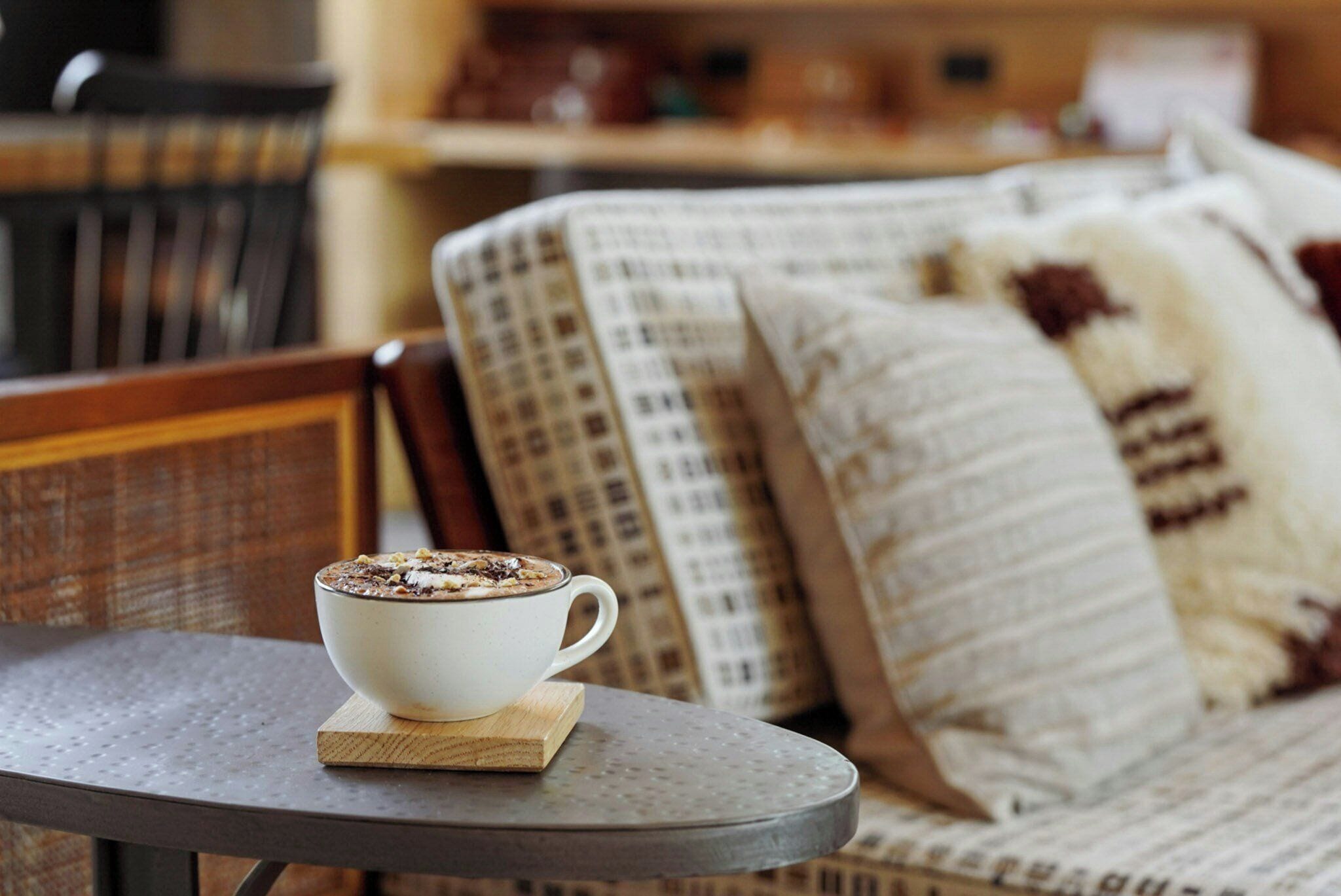 A white cup of coffee on a coaster on a round table.