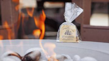 A bag of S'mores marshmallows, graham crackers, and dark chocolate on a table with a fire in the background.