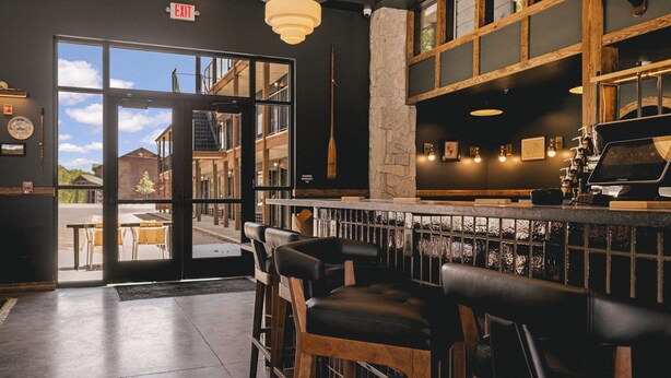 A bar area with wooden stools, a stone pillar, and a view through the glass door to the outside. - The Ozarker Lodge (Branson)