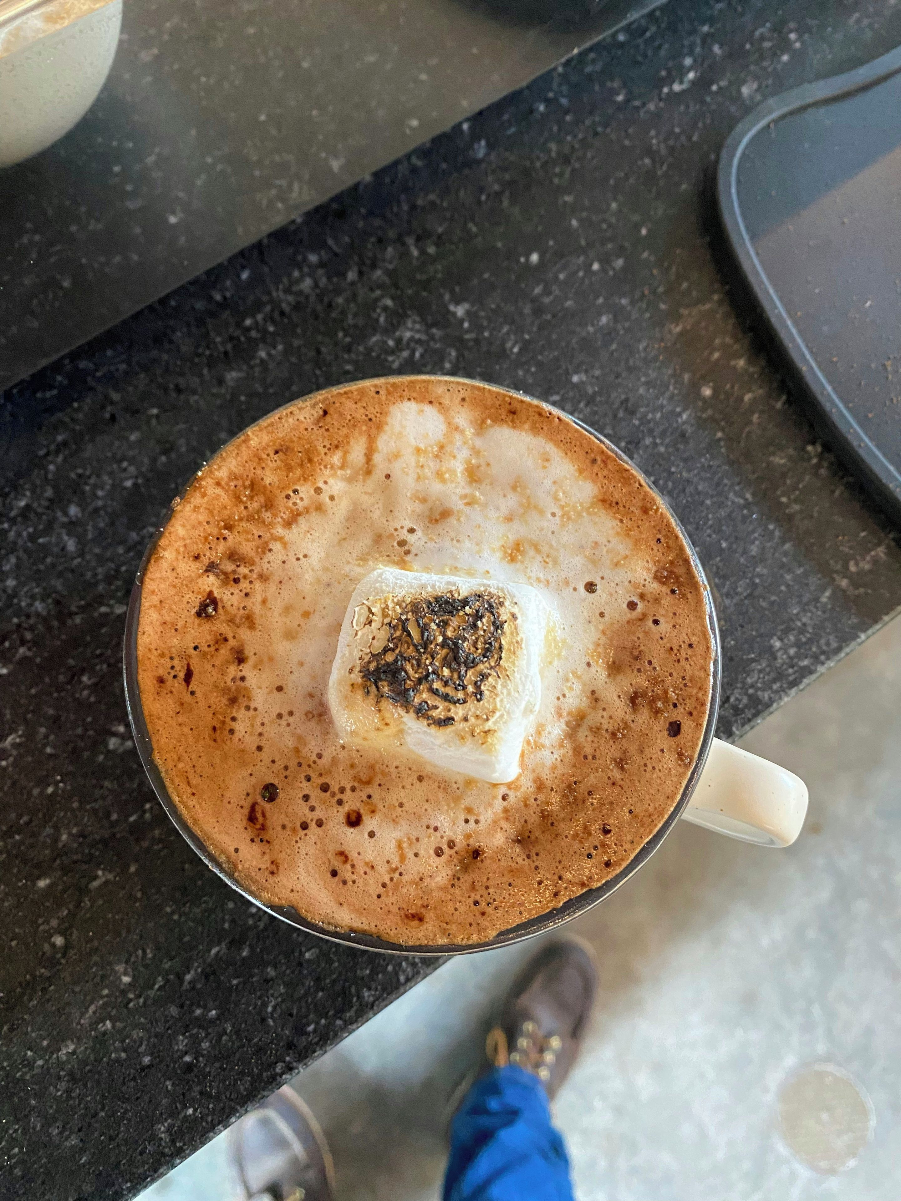 En kopp kaffe med ett skummande lager på toppen och en bit mat till.