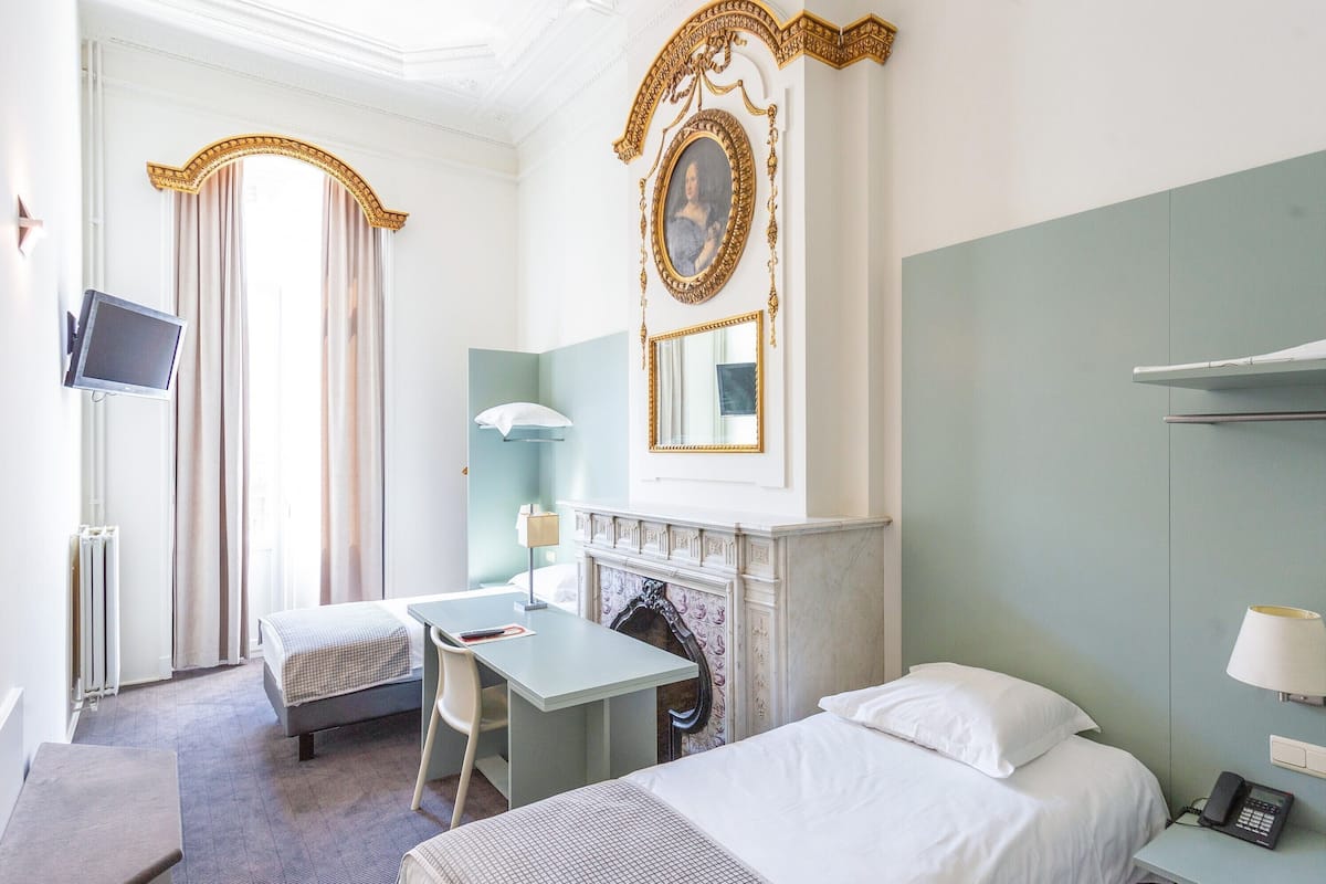 A hotel room with a bed, a desk, a chair, a fireplace, a television, and a mirror.
