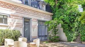 A building with a tiled facade, a covered patio with wicker furniture, and a staircase partially covered by greenery. - Hotel Du Congres (Brussels)