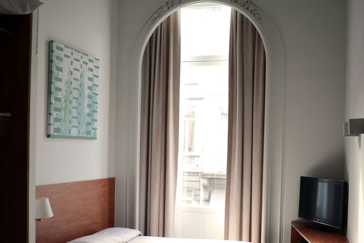 Habitación de hotel con cama, escritorio, silla, televisión y ventana con cortinas.