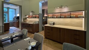A modern kitchen with wooden cabinets, a central island, and a dining area with a table set for two. - Hotel Du Congres (Brussels)