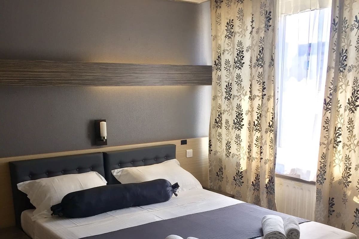 A neatly made double bed with a dark headboard, white bedding, and two rolled towels on the bed.
