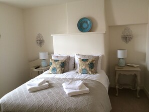 A neatly made bed with a patterned bedspread, two decorative pillows, and folded towels on the bed. There are two bedside tables with lamps and decorative items.