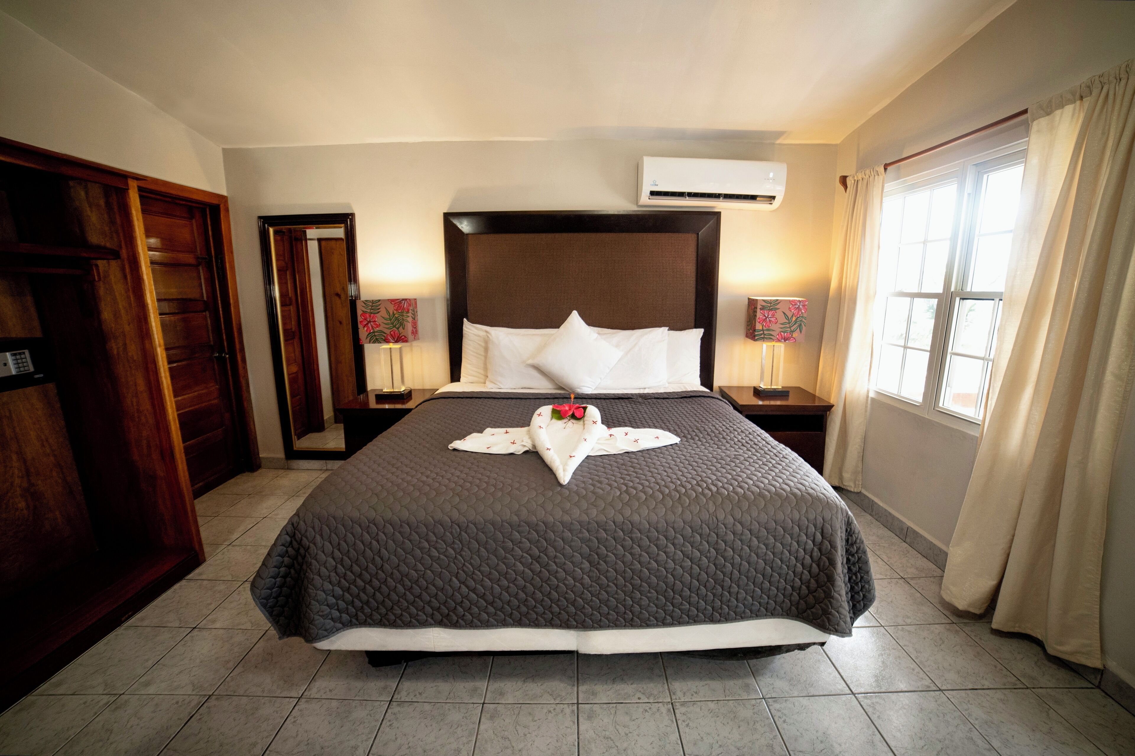 Hotelkamer met een groot bed, een houten garderobe, nachtkastjes met lampen, een airconditioningsysteem en een raam met gordijnen.