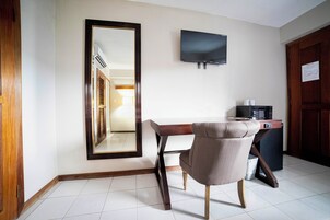 Hotelkamer met een houten bureau, een stoel, een flatscreen televisie aan de muur en een magnetron op een klein tafeltje.