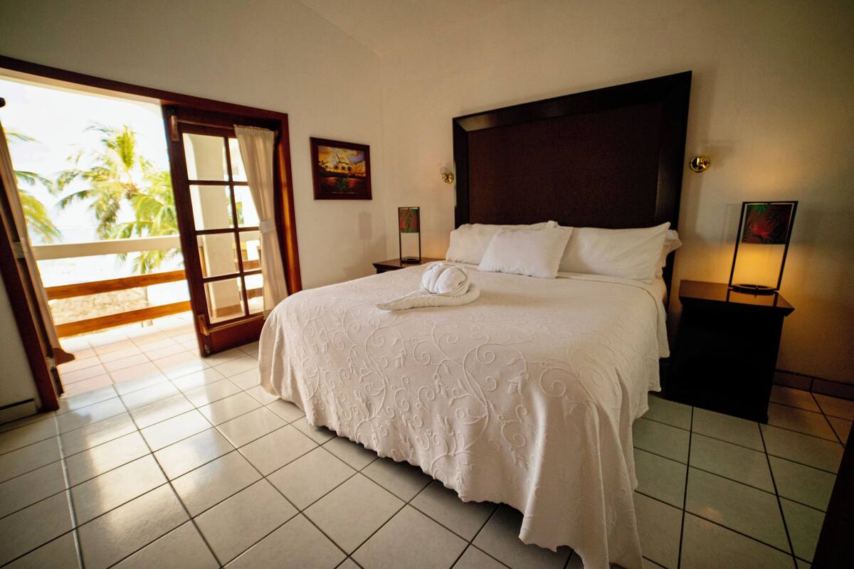 Une chambre d’hôtel comprenant un lit, une table de chevet, une porte donnant sur un espace extérieur et un mur orné de deux tableaux encadrés.