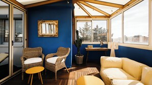 A sunroom with wicker furniture, a cactus, and a view of trees. - Hotel Le Petit Castel (Antibes)
