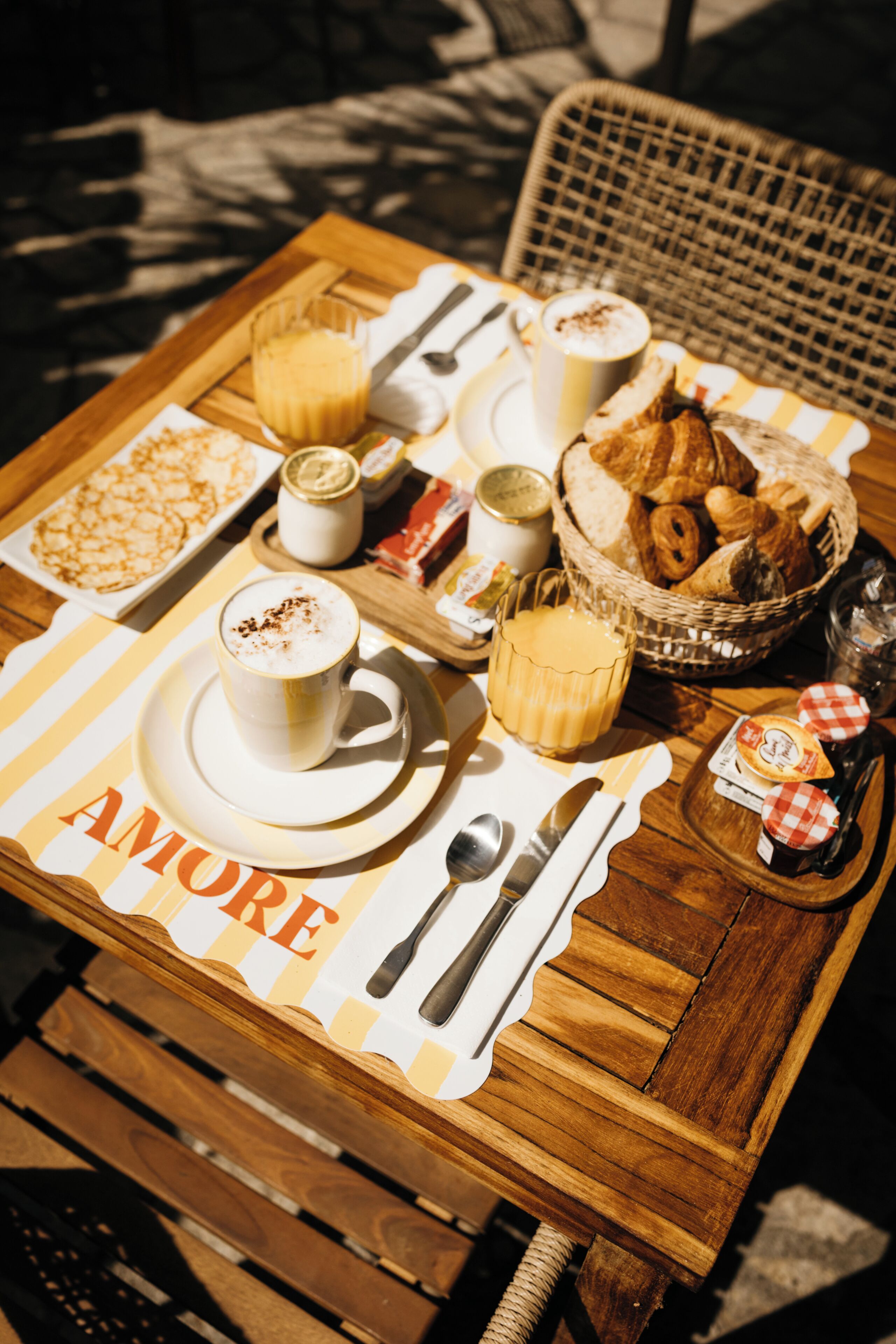Una mesa de madera con artículos de desayuno, incluyendo cruasanes, un cesto de pan y una taza de café.