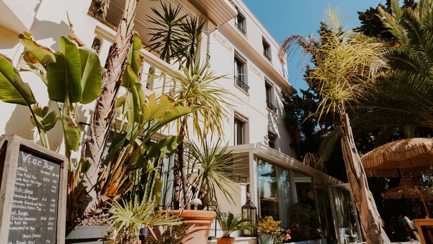 A building with a terrace, potted plants, and a signboard. - Hotel Le Petit Castel (Antibes)
