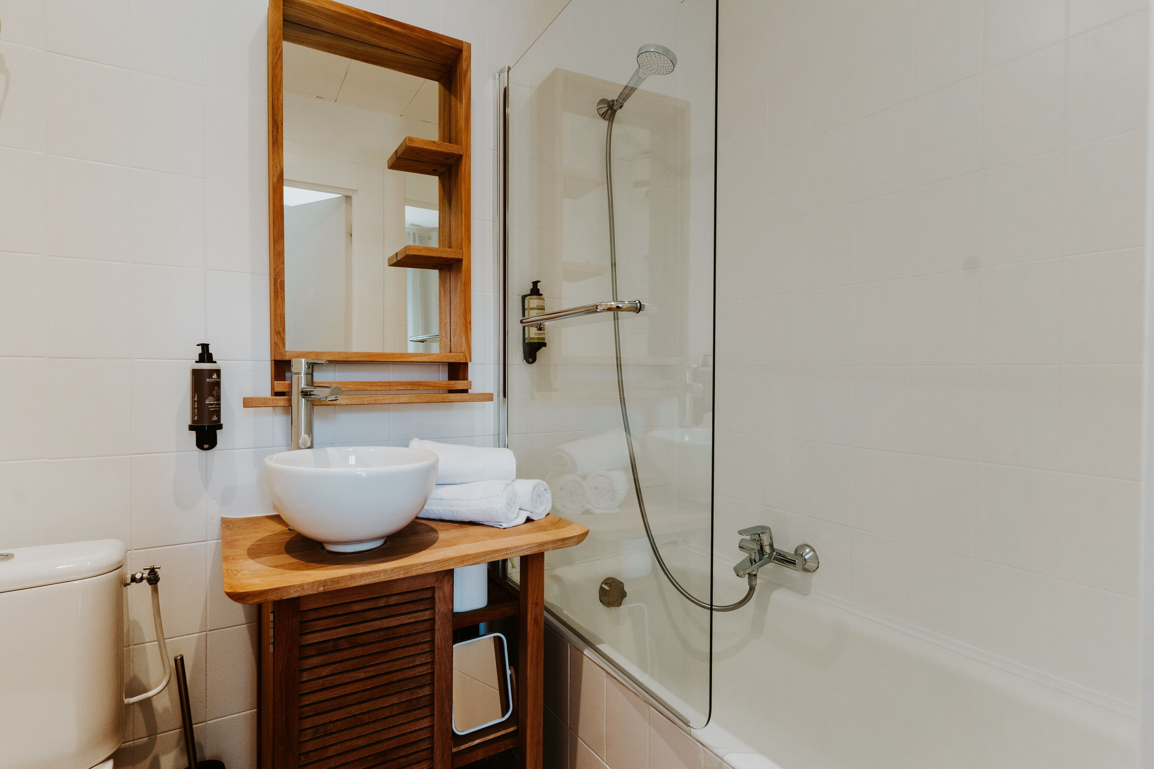 Un baño con tocador de madera, un espejo grande, un lavamanos blanco y una ducha con cerramiento de vidrio.