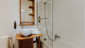 Un baño con tocador de madera, un espejo grande, un lavamanos blanco y una ducha con cerramiento de vidrio.