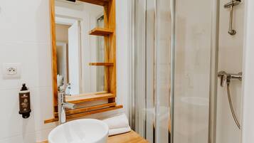 Un baño moderno con un espejo grande, un tocador de madera, un lavabo blanco y una cabina de ducha de vidrio.