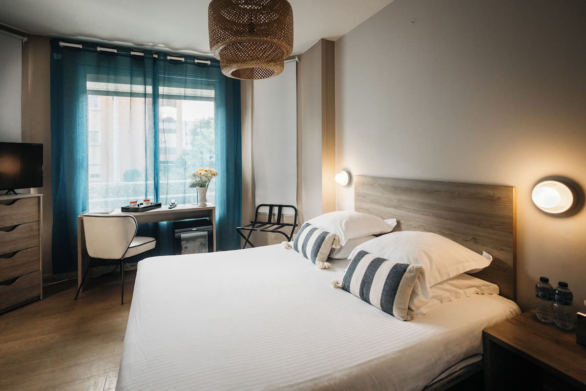 Quarto de hotel com cama, escrivaninha, cadeira e televisão.