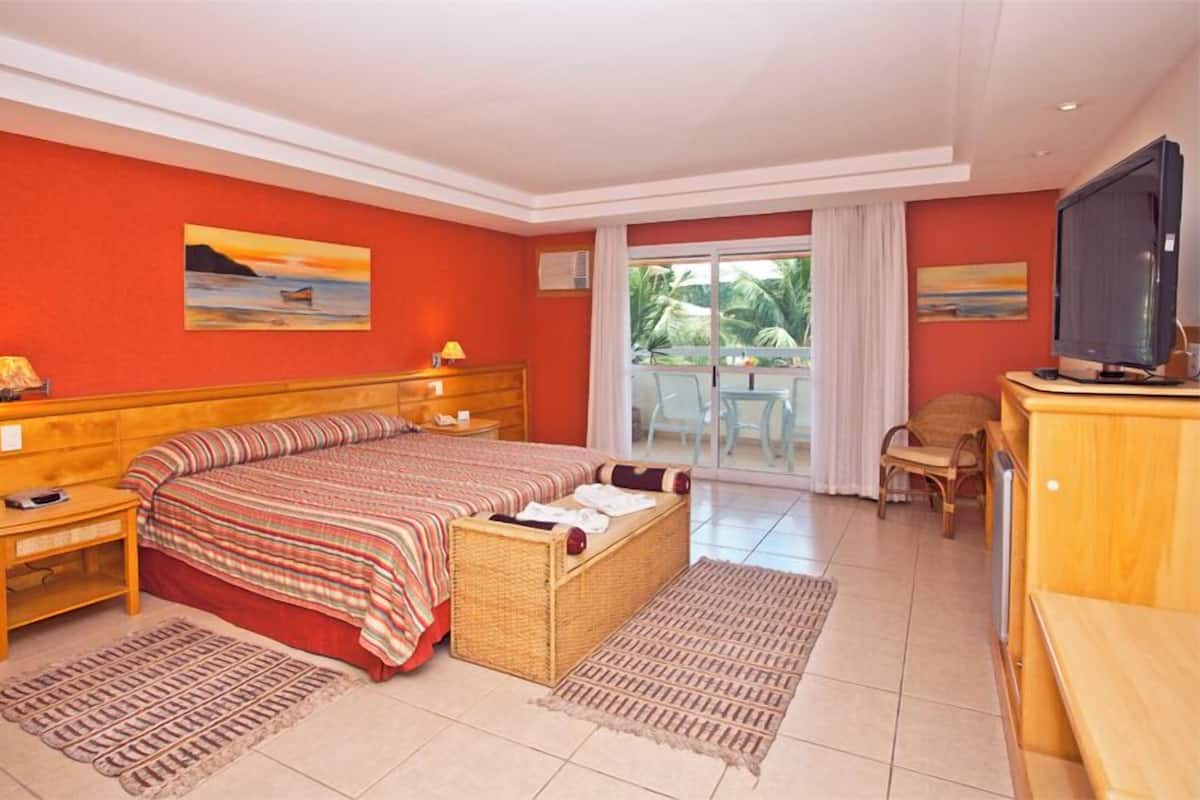Een hotelkamer met een bed, een televisie, een bureau en een balkon met uitzicht op palmbomen.