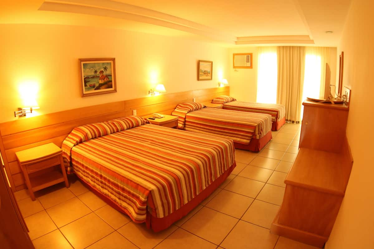 Een hotelkamer met drie bedden, een bureau en een televisie.