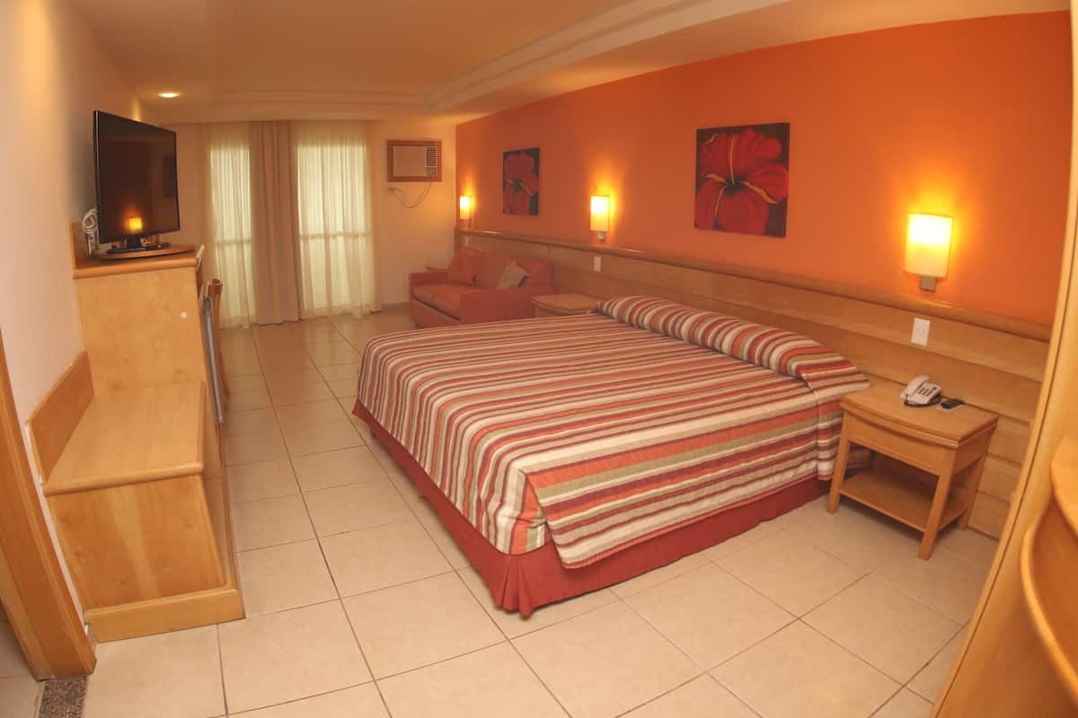 Een hotelkamer met een groot bed, een houten bureau, een televisie en twee wandlampen.
