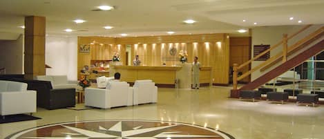 Un hall de hotel con mostrador de recepción, zona de estar y un gran emblema circular en el suelo.