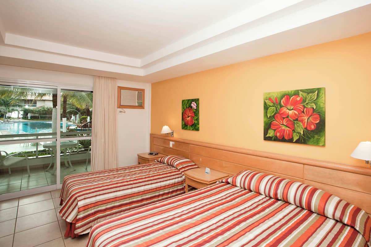 Een hotelkamer met twee bedden, uitzicht op een zwembad en twee schilderijen aan de muur.