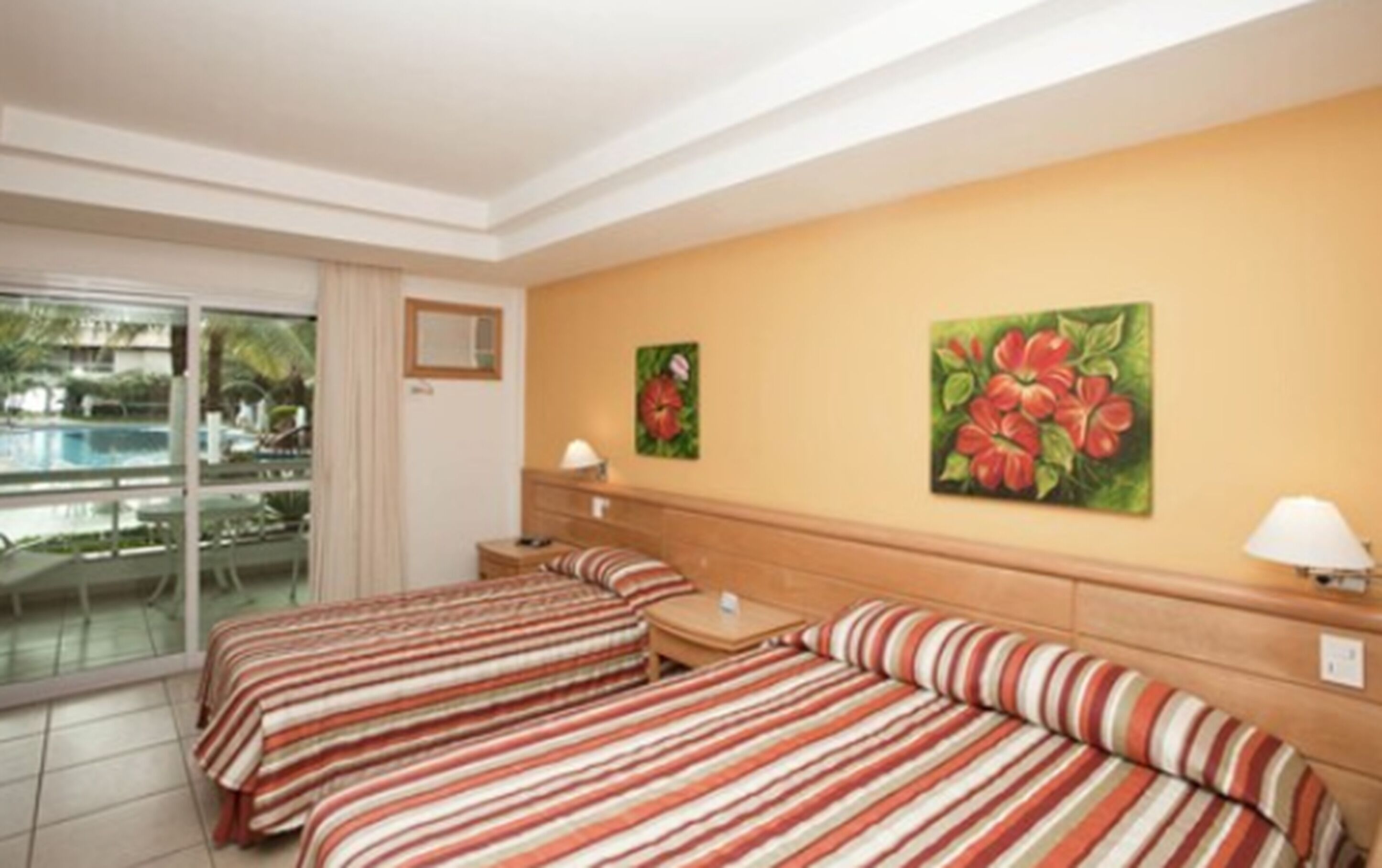 Une chambre d’hôtel avec deux lits, une petite table, une table de chevet et une fenêtre donnant sur une piscine.
