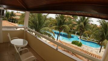 Uma varanda com vista para uma piscina, palmeiras e cadeiras de descanso.